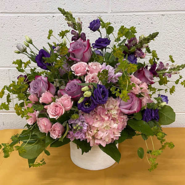 Pink and purple mixed flower arrangement in a white container