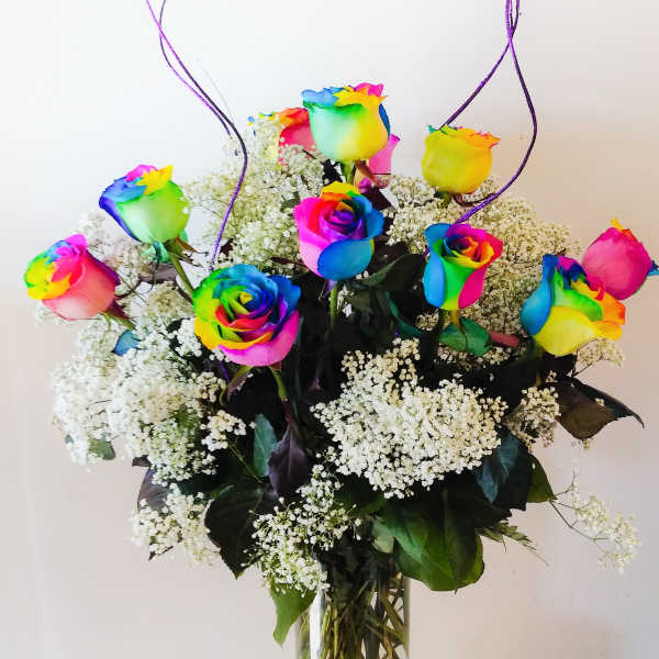 Rainbow-colored roses in a glass vase with white baby's breath