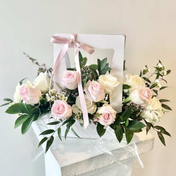Pink and white roses arranged in a white gift box with a pink ribbon