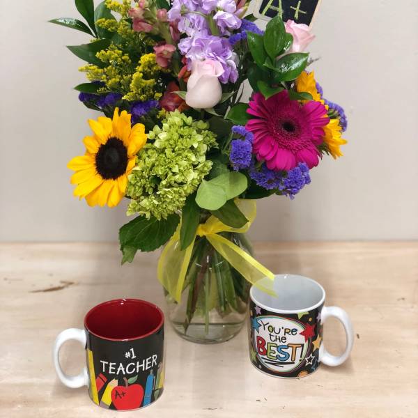 Mixed bouquet in a glass vase with two teacher-themed mugs in front