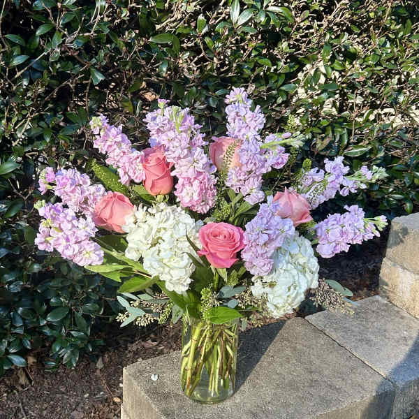 Pink roses and lavender flowers arranged in a clear glass vase