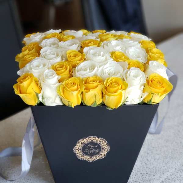 Yellow and white roses arranged in a black box with a ribbon