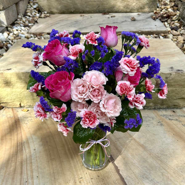 Pink roses and carnations in a glass vase with purple filler flowers