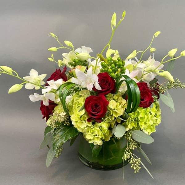Red roses and white orchids arranged with green hydrangeas in a glass vase
