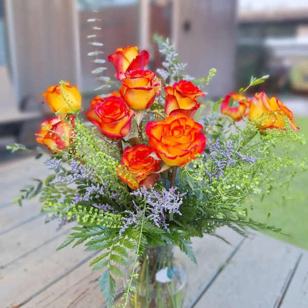 Orange and red roses in a glass vase with purple filler flowers