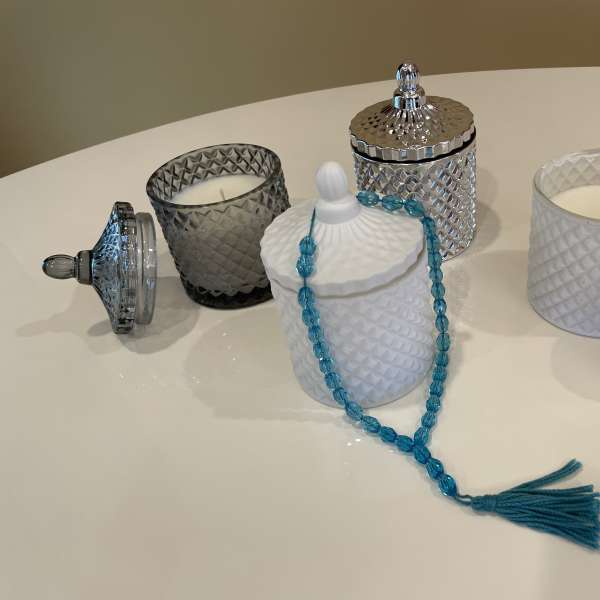Decorative glass candles and lidded jars on a table, with a blue bead strand draped over one jar.