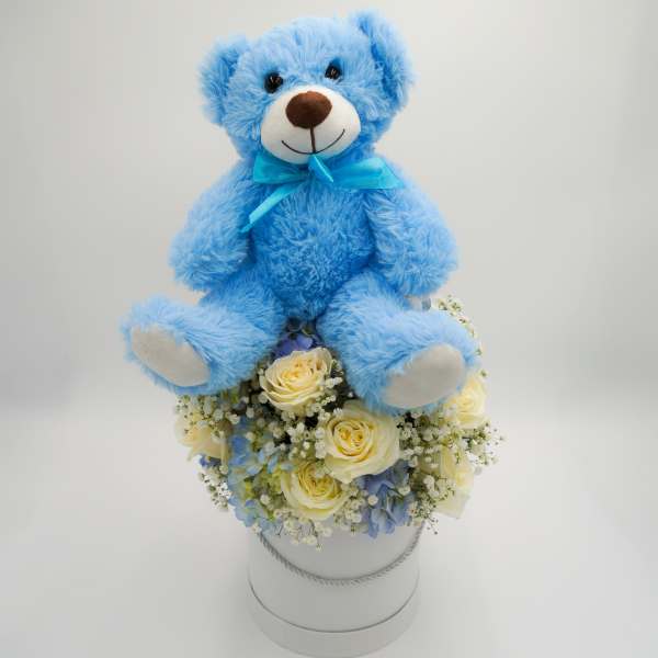 Blue teddy bear sitting on a bouquet in a white hatbox