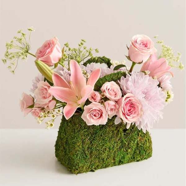 Pink roses and lilies arranged in a moss-covered container