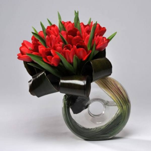 Red tulips arranged in a clear glass vase with a black ribbon