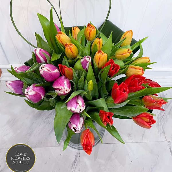 Multicolored tulip arrangement with orange, red, and purple blooms in a clear glass vase