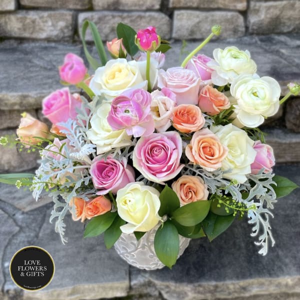 Pastel roses and ranunculus arranged in a white ceramic vase.