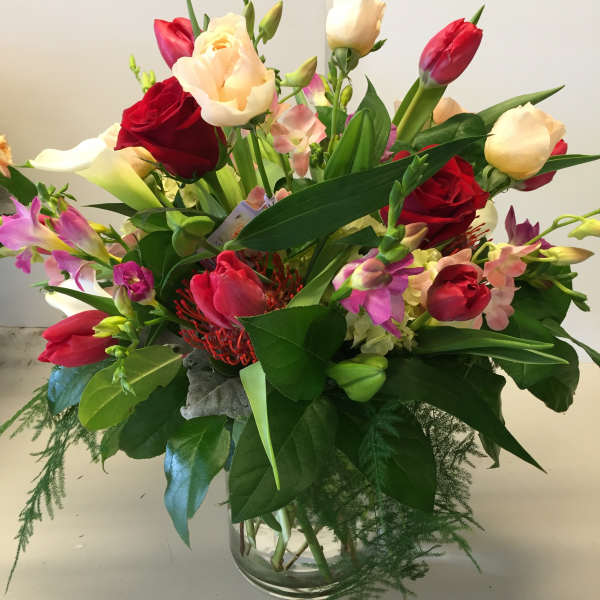 Mixed bouquet of roses, tulips, and orchids in a glass vase