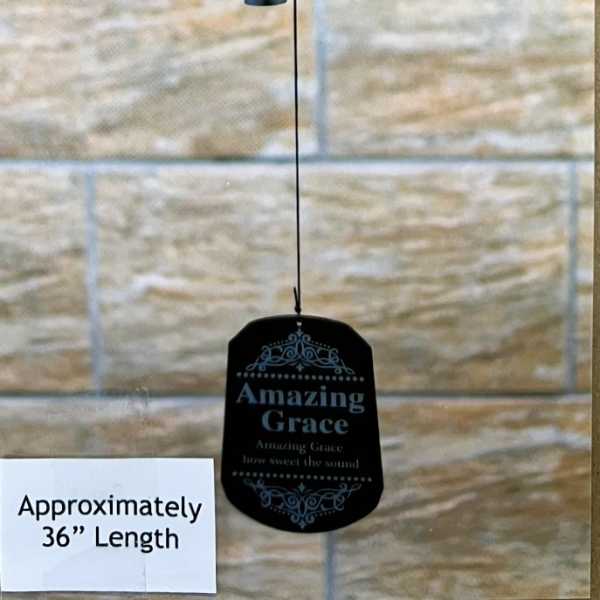 Black wind chime with silver text hanging against a stone wall