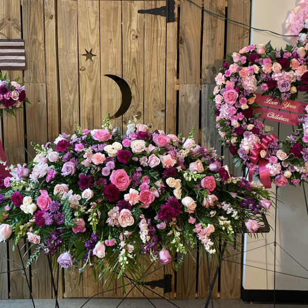 Pink and purple floral funeral display with a heart wreath and cross spray