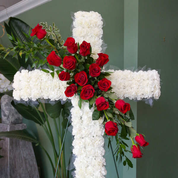 White floral cross with red roses on a stand