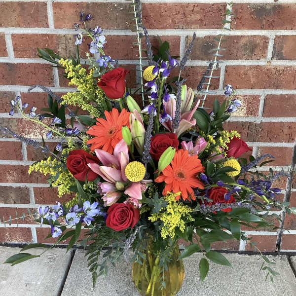 Mixed bouquet of red roses, lilies, and orange gerbera daisies in a glass vase