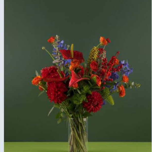 Tall mixed bouquet in a clear glass vase with red, orange, and blue flowers