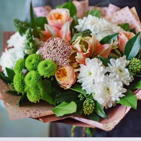 Handheld bouquet of peach and white flowers with green accents