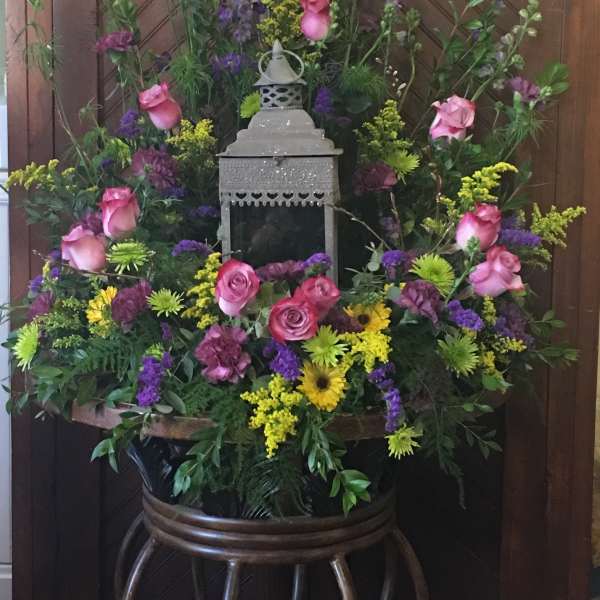 Large floral arrangement with pink roses, purple blooms, and yellow accents around a lantern