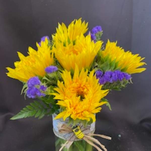 Yellow flowers and purple filler in a clear glass vase