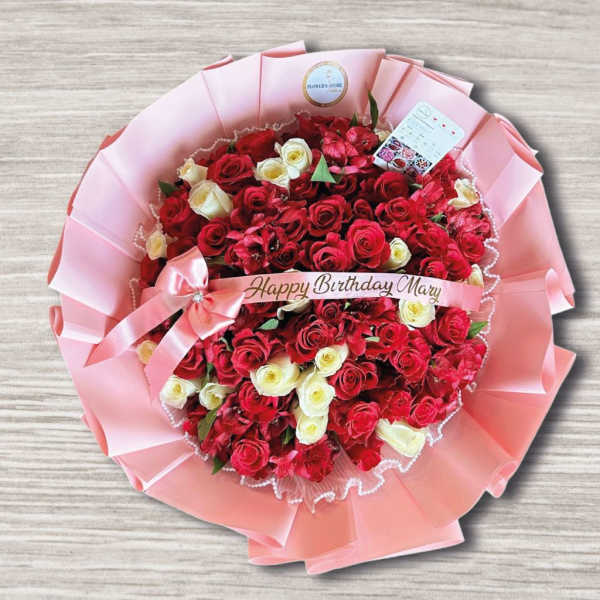 Round bouquet of red and white roses wrapped in pink paper with a birthday ribbon