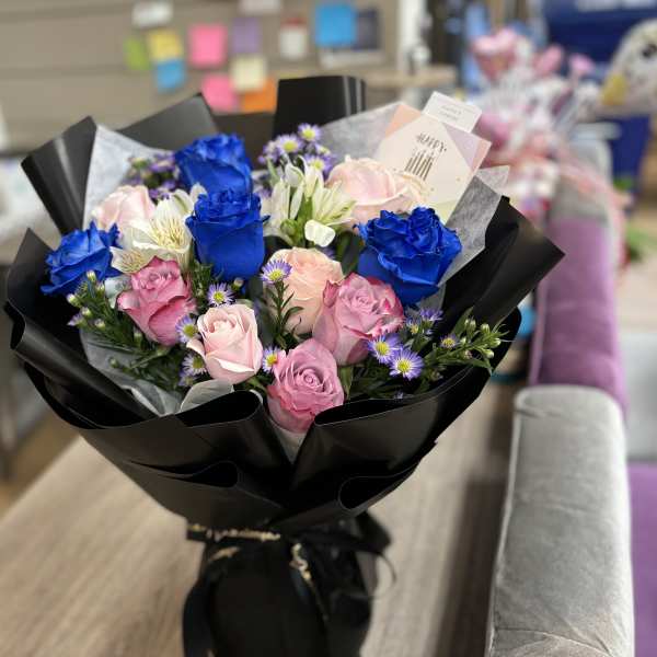Bouquet of blue and pink roses with small purple flowers in black wrap