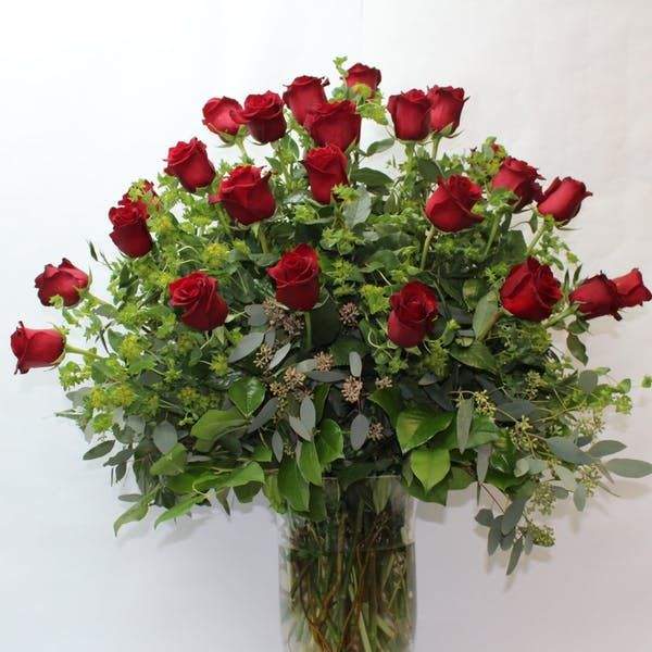 Red roses arranged in a tall glass vase with greenery