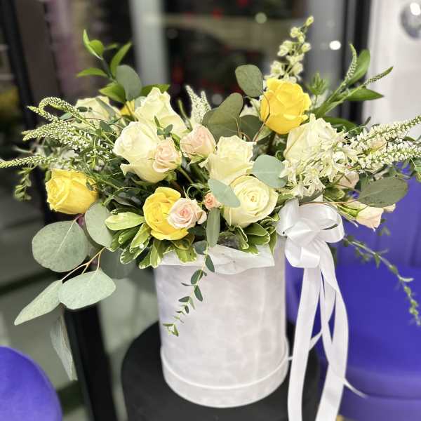 Yellow and white roses arranged in a white hat box with a ribbon