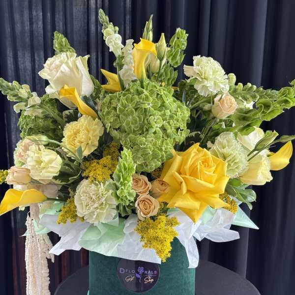 Yellow and white floral arrangement in a green hatbox