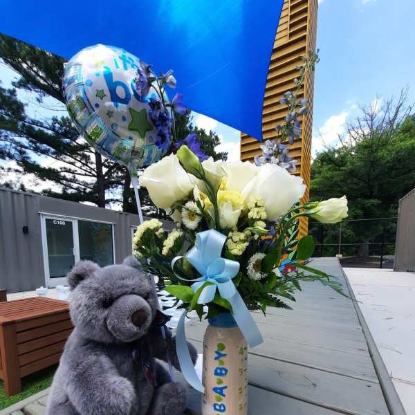 Bouquet of white and pale yellow flowers in a decorated bottle with a teddy bear and baby balloon