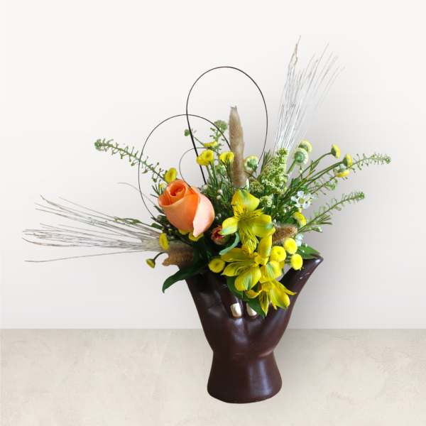 Orange and yellow floral arrangement in a dark hand-shaped vase