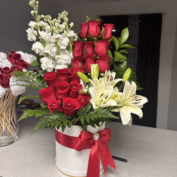 Red roses and white lilies arranged in a white hat box with a red ribbon