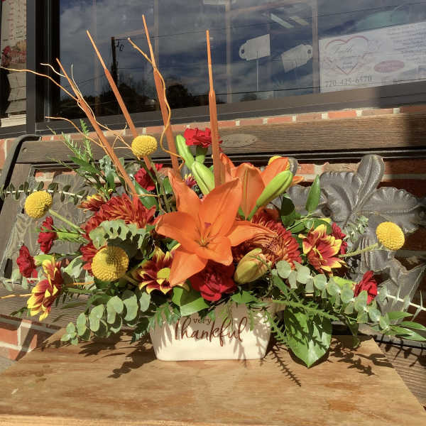 Orange lily and mixed flowers in a cream container