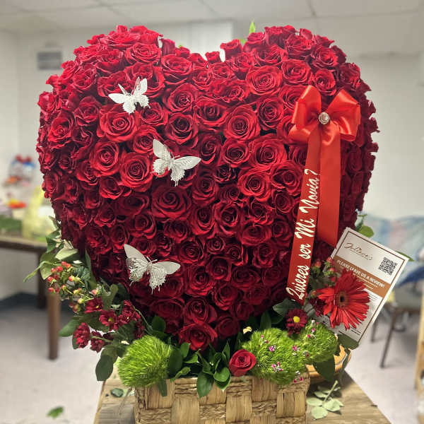 Heart-shaped red rose arrangement in a woven basket with a red ribbon