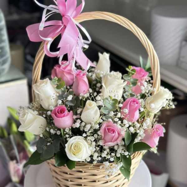 Pink and white roses arranged in a wicker basket with a ribbon bow