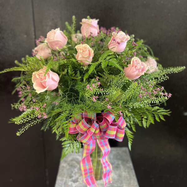 Pink roses in a glass vase with a colorful plaid ribbon
