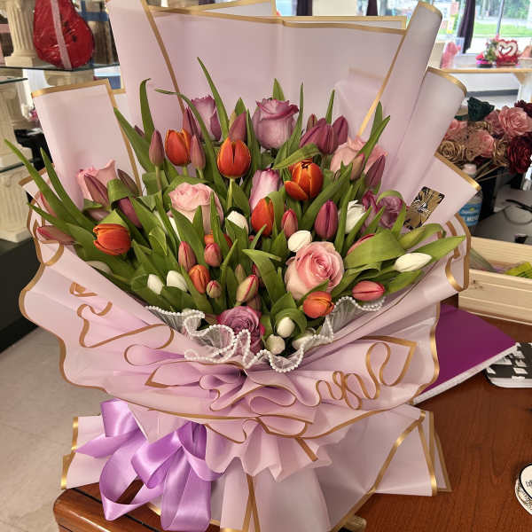 Bouquet of pink, purple, and orange tulips with roses wrapped in pink paper