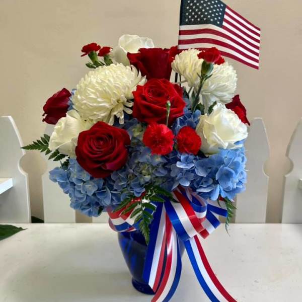 Red and white roses with blue hydrangeas in a vase, topped with an American flag