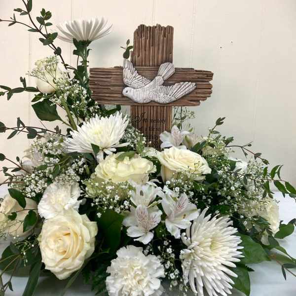 White floral arrangement with roses and daisies around a wooden cross