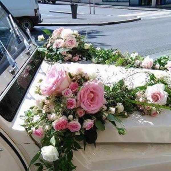 Pink and white floral arrangement draped over a car hood