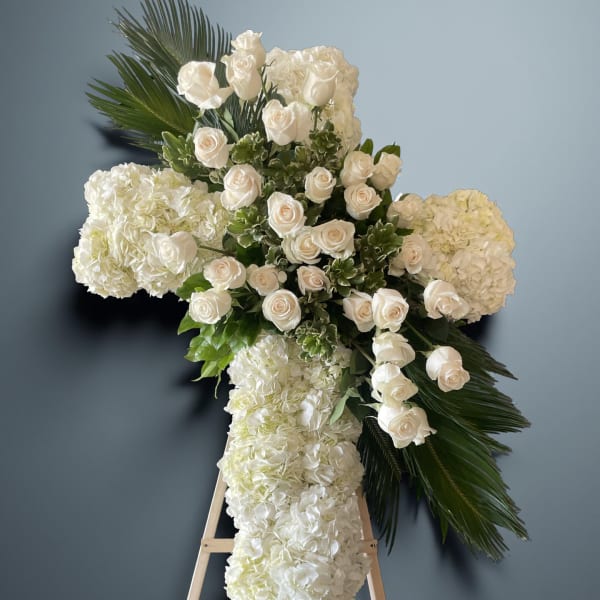White floral cross on an easel with roses and hydrangeas