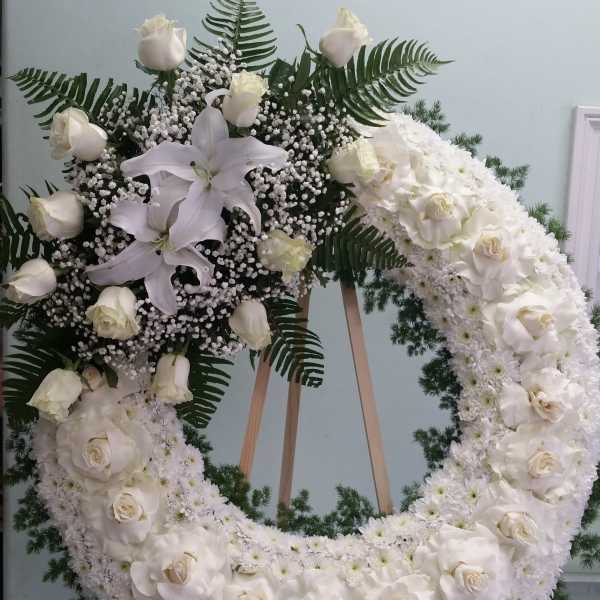 White floral wreath with roses, lilies, and fern accents on an easel