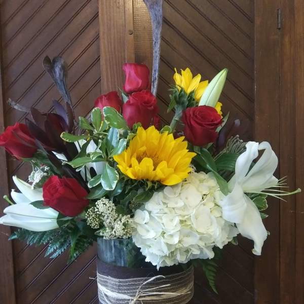 Tall bouquet of red roses, white lilies, yellow sunflower, and white hydrangea in a glass vase