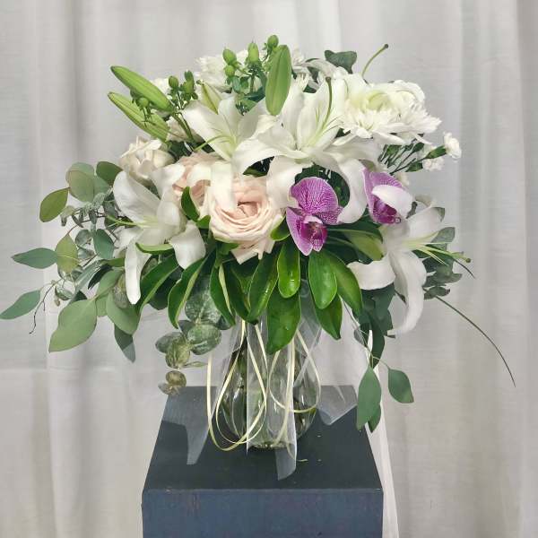 White lilies and roses in a glass vase with purple orchids