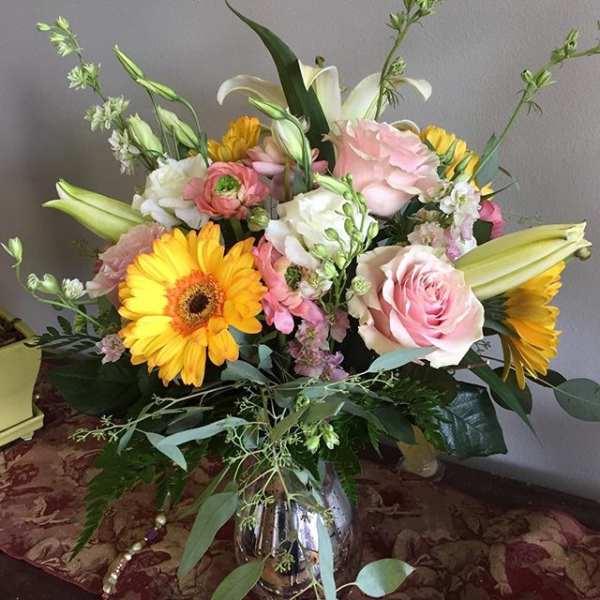Mixed bouquet with pink roses, yellow gerbera daisies, and white lilies in a silver vase