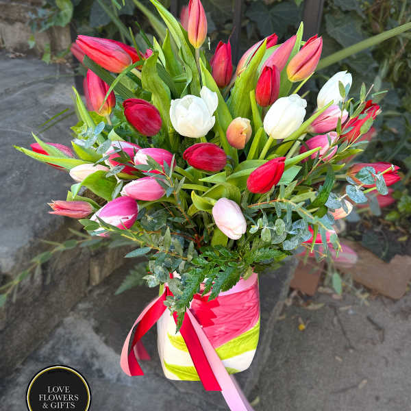 Tall arrangement of red, pink, white, and peach tulips in a striped vase with ribbons