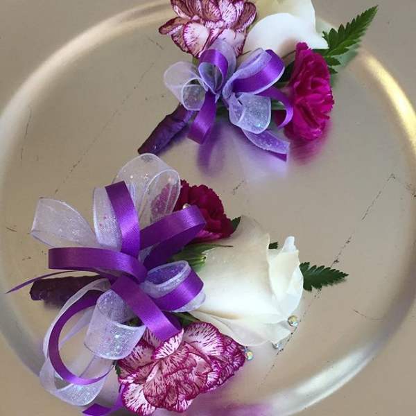Two purple and white floral corsages with ribbon on a plate