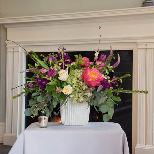 Large floral arrangement in a white vase with pink, purple, and white blooms