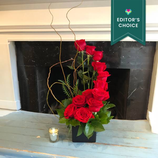 Tall arrangement of red roses in a black vase with a small candle nearby