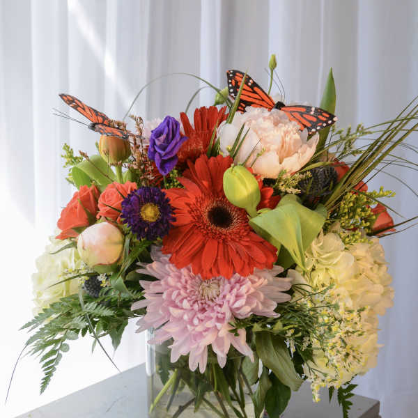 Mixed bouquet in a glass vase with bright flowers and butterfly accents